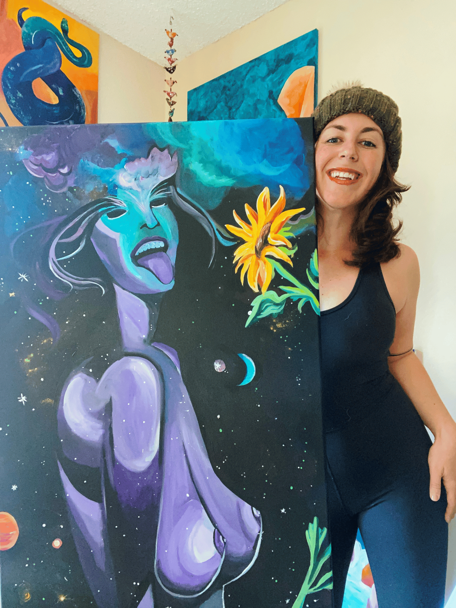 image of Kate DeCoste holding up her painting of a nake woman, her tongue sticking out in space with a sunflower